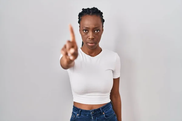 Beautiful black woman standing over isolated background pointing with finger up and angry expression, showing no gesture