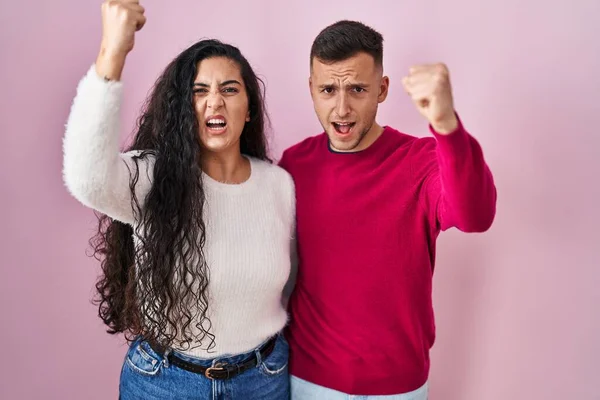 Young Hispanic Couple Standing Pink Background Angry Mad Raising Fist — Stockfoto