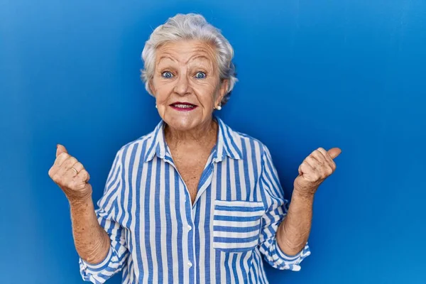 站在蓝色背景上的白发苍苍的老妇人 高举双臂 睁大眼睛 为成功感到惊奇和惊奇 获奖者概念 — 图库照片
