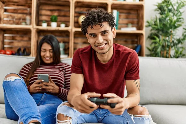 Man playing video game and woman using smartphone at home.