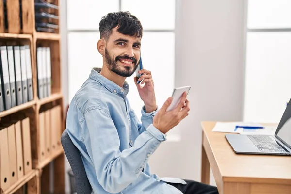 Νεαρός Ισπανόφωνος Επιχειρηματίας Μιλώντας Στο Smartphone Ανάγνωση Σημειωματάριο Στο Γραφείο — Φωτογραφία Αρχείου