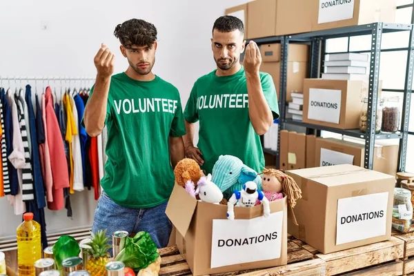 Young gay couple wearing volunteer t shirt at donations stand doing italian gesture with hand and fingers confident expression