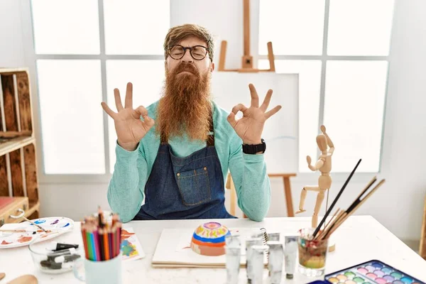 红头发的男人 留着长胡子 在艺术工作室里画着黏土碗 微笑着闭上双眼 用手指做冥想动作 瑜伽概念 — 图库照片