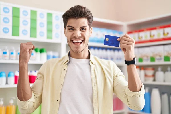 Young Hispanic Man Pharmacy Drugstore Holding Credit Card Screaming Proud — Stock Photo, Image