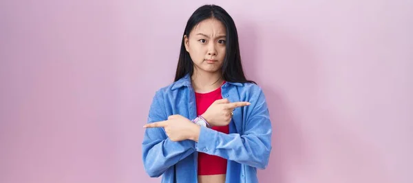 Jonge Aziatische Vrouw Staan Roze Achtergrond Wijzend Naar Beide Zijden — Stockfoto