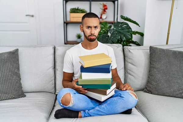 African American Young Man Holding Pile Books Sitting Sofa Depressed — Foto de Stock