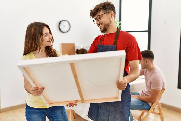 Group of people drawing sitting on the table. Man and woman smiling happy holding canvas at art studio.