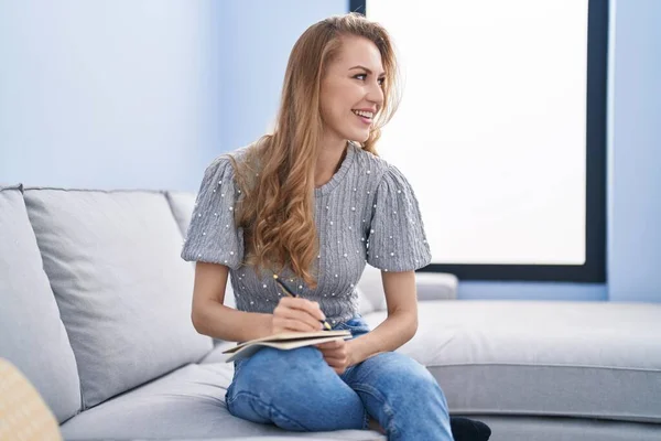 Ung Blondine Kvinde Skriver Notesbog Sidder Sofaen Derhjemme - Stock-foto