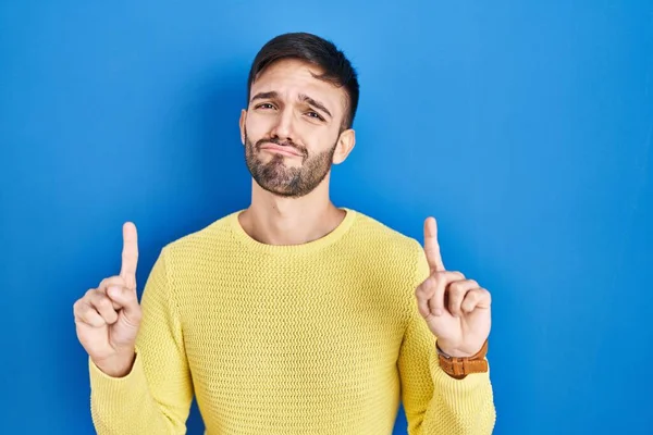一个西班牙裔男子站在蓝色的背景上 面带微笑地抬起头 用手指指示方向 他不快乐 情绪低落 — 图库照片