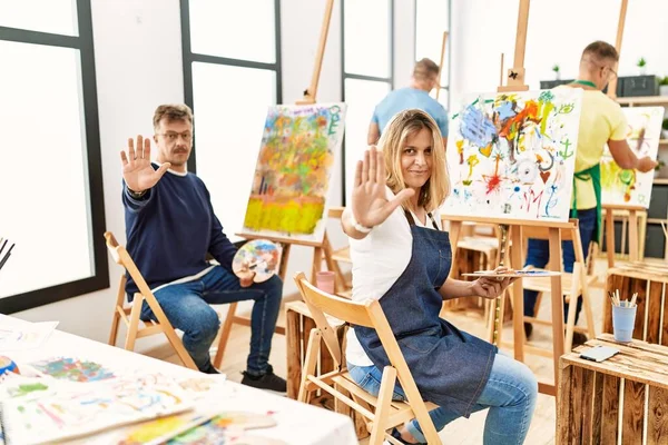 Group of middle age artist at art studio doing stop sing with palm of the hand. warning expression with negative and serious gesture on the face.