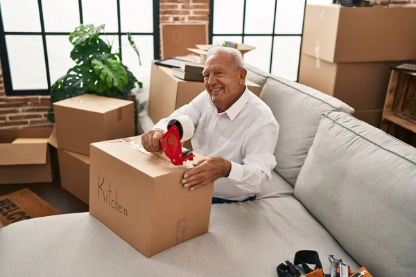 Senior man smiling confident packing cardobard box at new home
