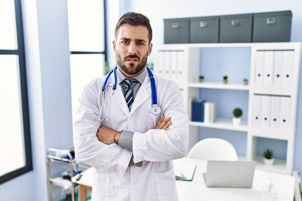 Handsome hispanic man wearing doctor uniform and stethoscope at medical clinic skeptic and nervous, disapproving expression on face with crossed arms. negative person. 