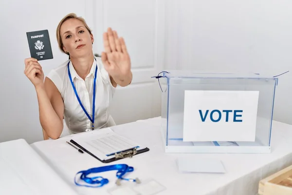 Young blonde woman at political campaign election holding usa passport with open hand doing stop sign with serious and confident expression, defense gesture