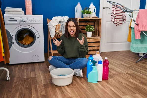 Young hispanic woman doing laundry washing by hand crazy and mad shouting and yelling with aggressive expression and arms raised. frustration concept.