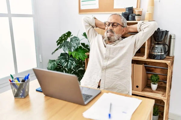 Senior grey-haired man relaxed with hands on head working at office