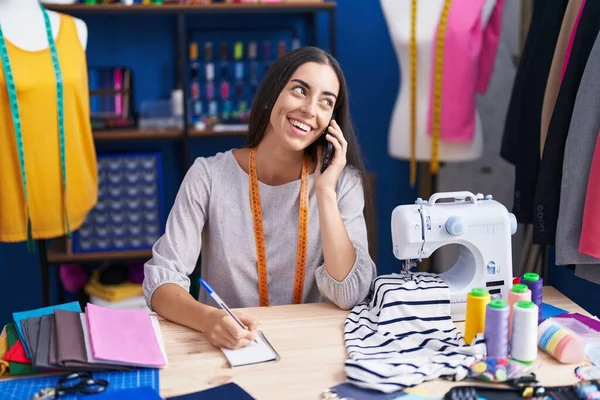 Young Beautiful Hispanic Woman Tailor Talking Smartphone Writing Notebook Clothing — Stockfoto