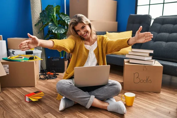 年轻女人坐在新家的地板上 用笔记本电脑看着摄像机 张开双臂拥抱 欢快的表达拥抱幸福 — 图库照片