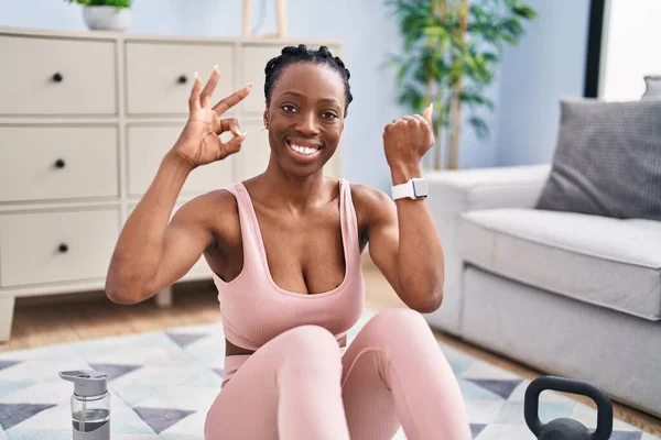Beautiful black woman using smart watch training at home doing ok sign with fingers, smiling friendly gesturing excellent symbol