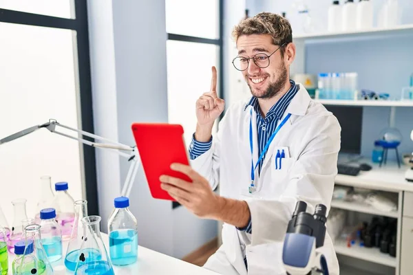 Hispanic man with beard working at scientist laboratory doing video call smiling with an idea or question pointing finger with happy face, number one