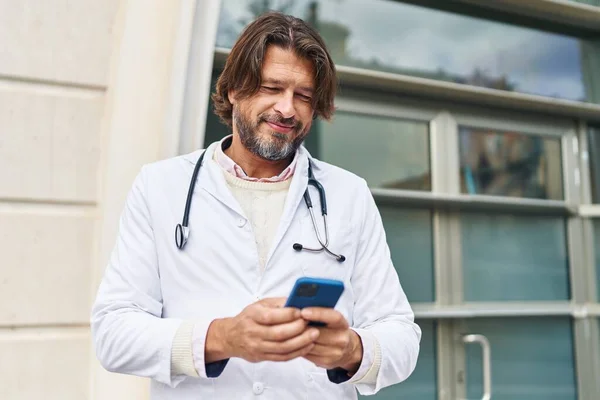 Hastanedeki Akıllı Telefonu Kullanarak Gülümseyen Orta Yaşlı Bir Doktor — Stok fotoğraf