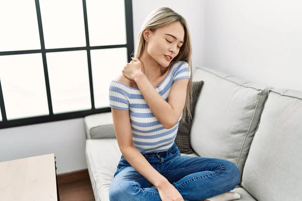 Young chinese woman with neck pain sitting on the sofa at home