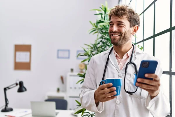 Young Hispanic Man Wearing Doctor Uniform Using Smartphone Drinking Coffee — Stock Photo, Image