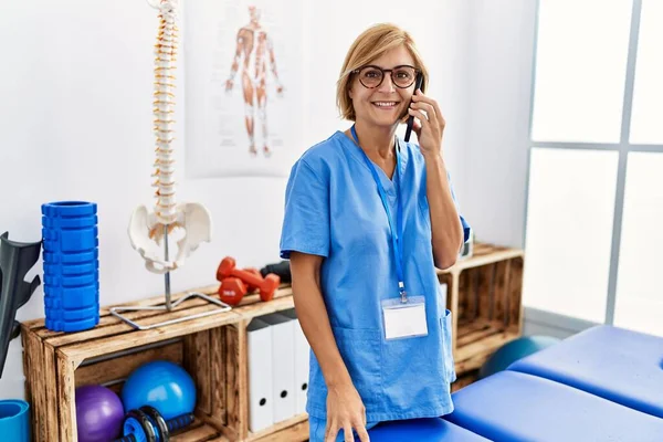 Mujer Rubia Mediana Edad Con Uniforme Fisioterapeuta Hablando Teléfono Inteligente —  Fotos de Stock