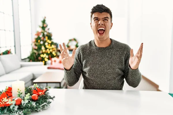 Mladý Hispánec Sedící Stole Vánočního Stromku Šílený Šílený Křičící Křičící — Stock fotografie