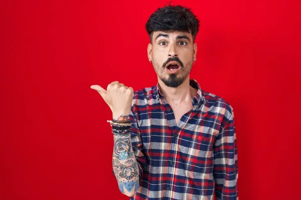 Jovem Hispânico Homem Com Barba Sobre Fundo Vermelho Surpreso Apontando — Fotografia de Stock