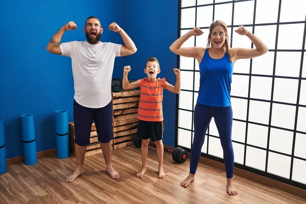 Family of three wearing sportswear at the gym angry and mad screaming frustrated and furious, shouting with anger looking up.