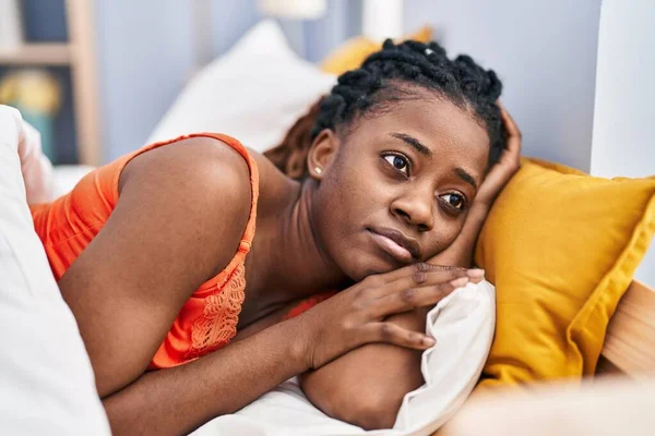 African american woman lying on bed with serious expression at bedroom