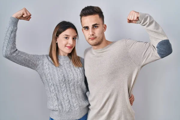 Young Hispanic Couple Standing White Background Strong Person Showing Arm — Stockfoto