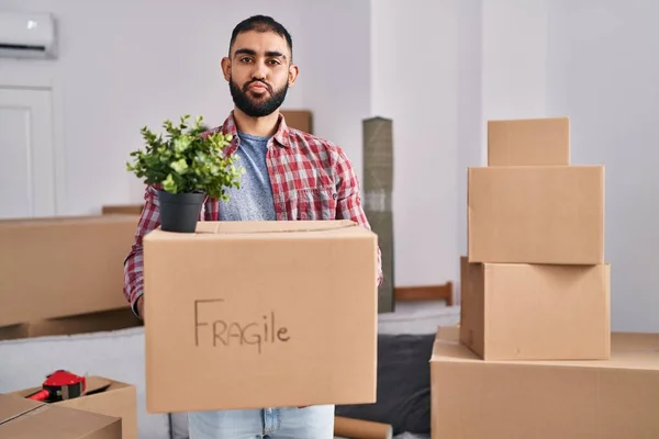 Middle east man with beard moving to a new home holding cardboard box looking at the camera blowing a kiss being lovely and sexy. love expression.