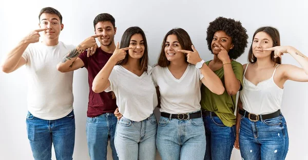 Group of young friends standing together over isolated background pointing with hand finger to face and nose, smiling cheerful. beauty concept