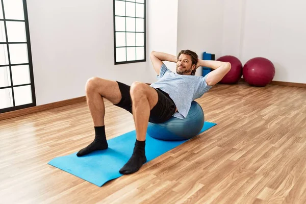 Middle age caucasian man smiling confident training using fit ball at sport center