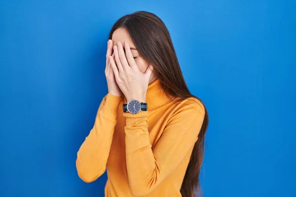 泣きながら手で顔を覆う悲しい表情で青い背景の上に立つ若いブルネットの女性 うつ病の概念 — ストック写真