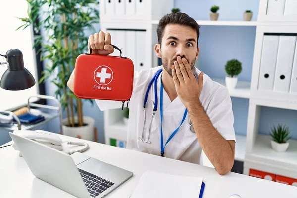 Young Hispanic Doctor Man Holding First Aid Kit Covering Mouth — Stock Photo, Image