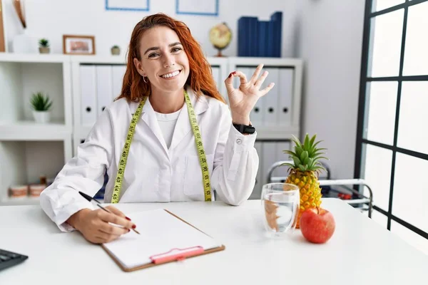 Klinikteki Genç Kızıl Saçlı Kadın Beslenme Uzmanı Olumlu Gülümsüyor Parmaklarıyla — Stok fotoğraf