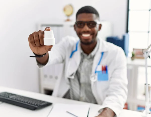 Young african american doctor man wearing doctor uniform holding prescription pills at the clinic looking positive and happy standing and smiling with a confident smile showing teeth