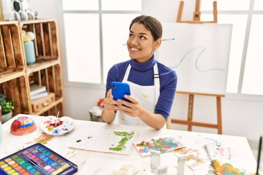 Sanat stüdyosunda akıllı telefon çizimi yapan genç Latin bir kadın.