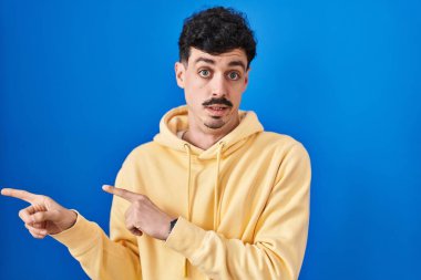 Mavi arka planda dikilen İspanyol bir adam iki eliyle endişeli ve gergin bir ifadeye işaret ediyor. 