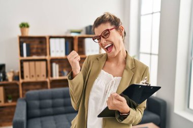 Muayenehanede çalışan genç bir kadın çok mutlu ve heyecanlı bir şekilde kollarını kaldırmış, gülümseyen ve başarı çığlıkları atan bir jest yapıyor. kutlama konsepti. 