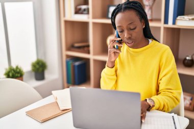 African american woman using laptop talking on smartphone at home