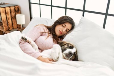 Genç bir kadın yatak odasında bir köpekle yatakta uyuyor.