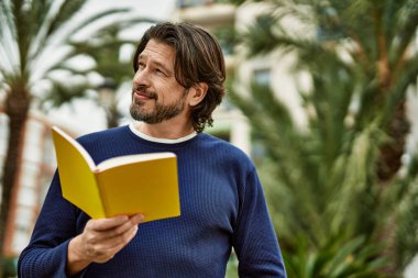 Orta yaşlı yakışıklı bir adam parkta kitap okuyor.