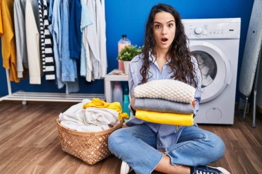 Genç esmer kadın temiz çamaşırları şok olmuş suratıyla tutuyor, şüpheci ve alaycı görünüyor, ağzı açık kalınca şaşırıyor. 