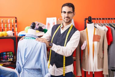 Young hispanic man tailor smiling confident measuring shirt at atelier