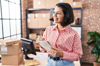 Genç kadın ecommerce iş işçisi ofiste deftere yazıyor.