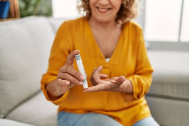 Orta yaşlı beyaz kadın evdeki kanepede oturmuş glikoz ölçüyor..