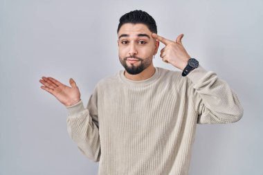 İzole edilmiş arka planda duran genç yakışıklı adam avuç içi boşluğunun fotokopi alanını göstermesi ve alnını işaret etmesi kafasını karıştırmış ve sinirlenmiş. Bunu bir düşün.. 